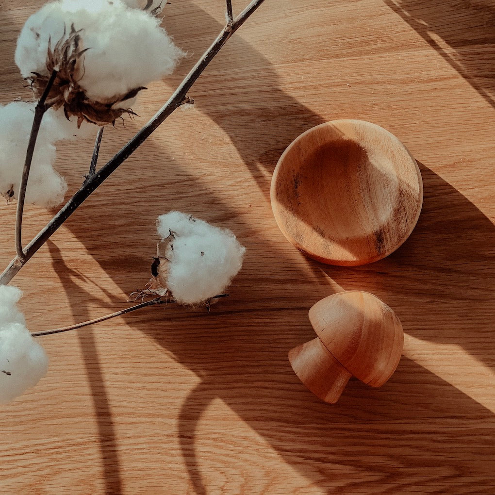 an image of a wooden mortar and pestle herb crusher laying on a timber background with fluffy white cotton flowers next to it
