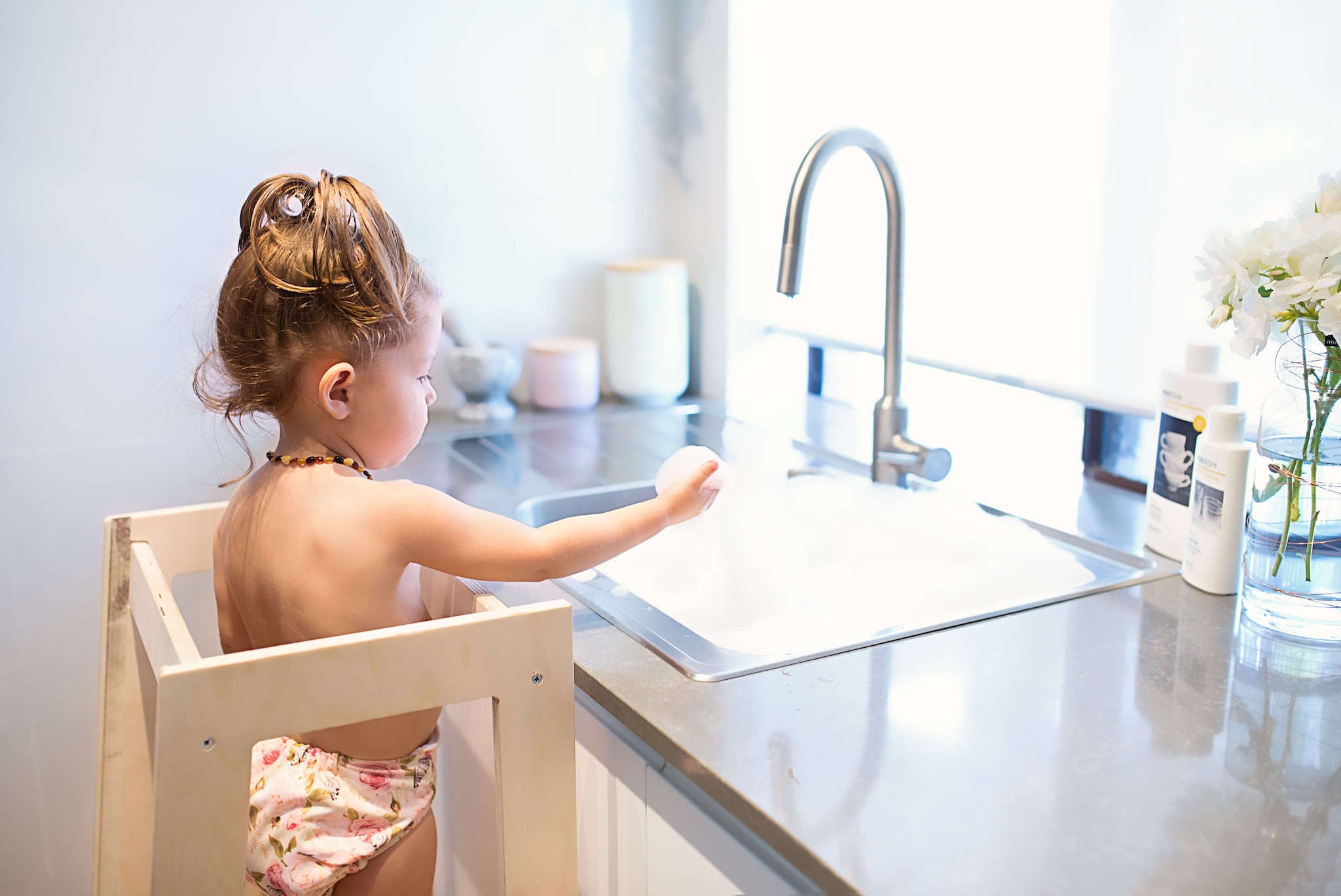 child in a learning tower washing dishes