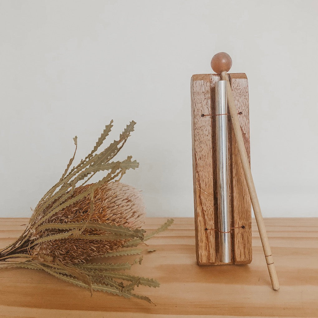 an image of wooden chime bar instrument standing upright on a timber bench top with a dried native flower  next to it