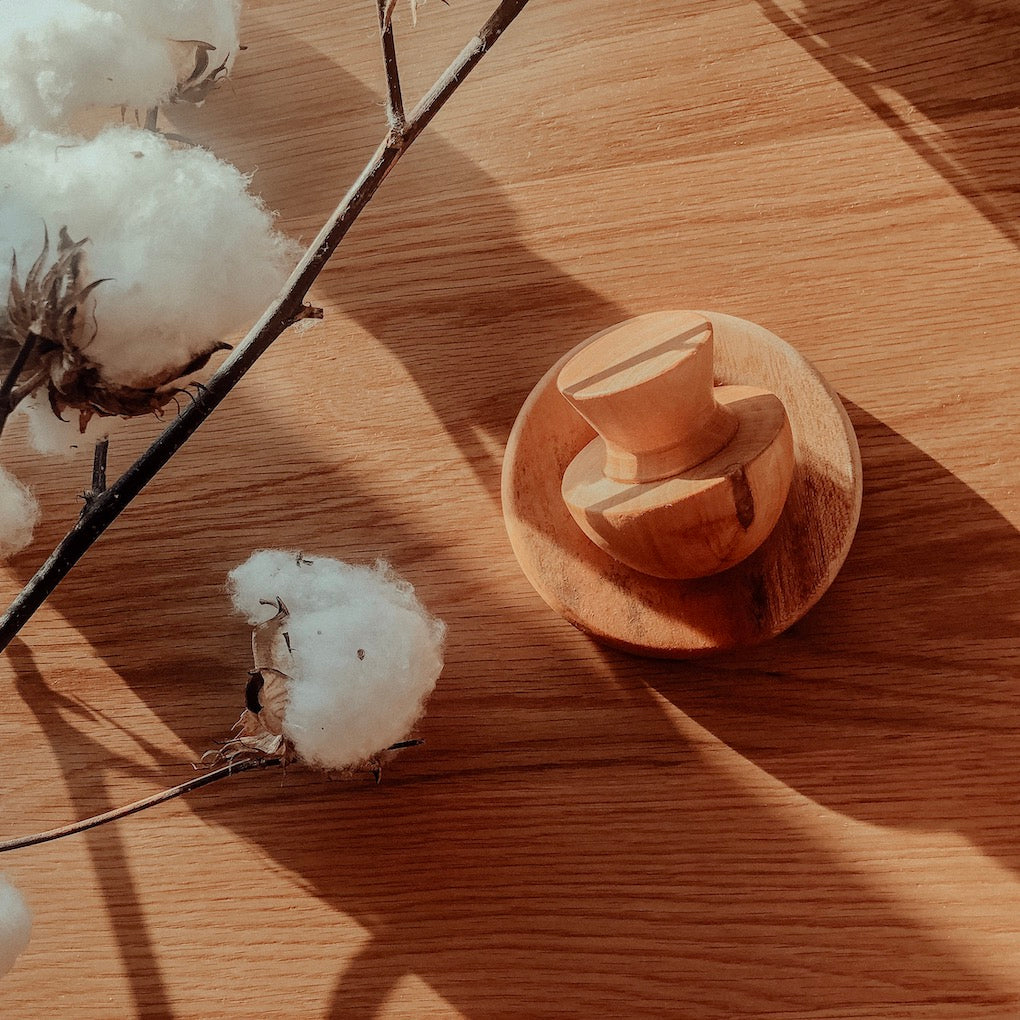 an image of a wooden mortar and pestle herb crusher laying on a timber background with fluffy white cotton flowers next to it